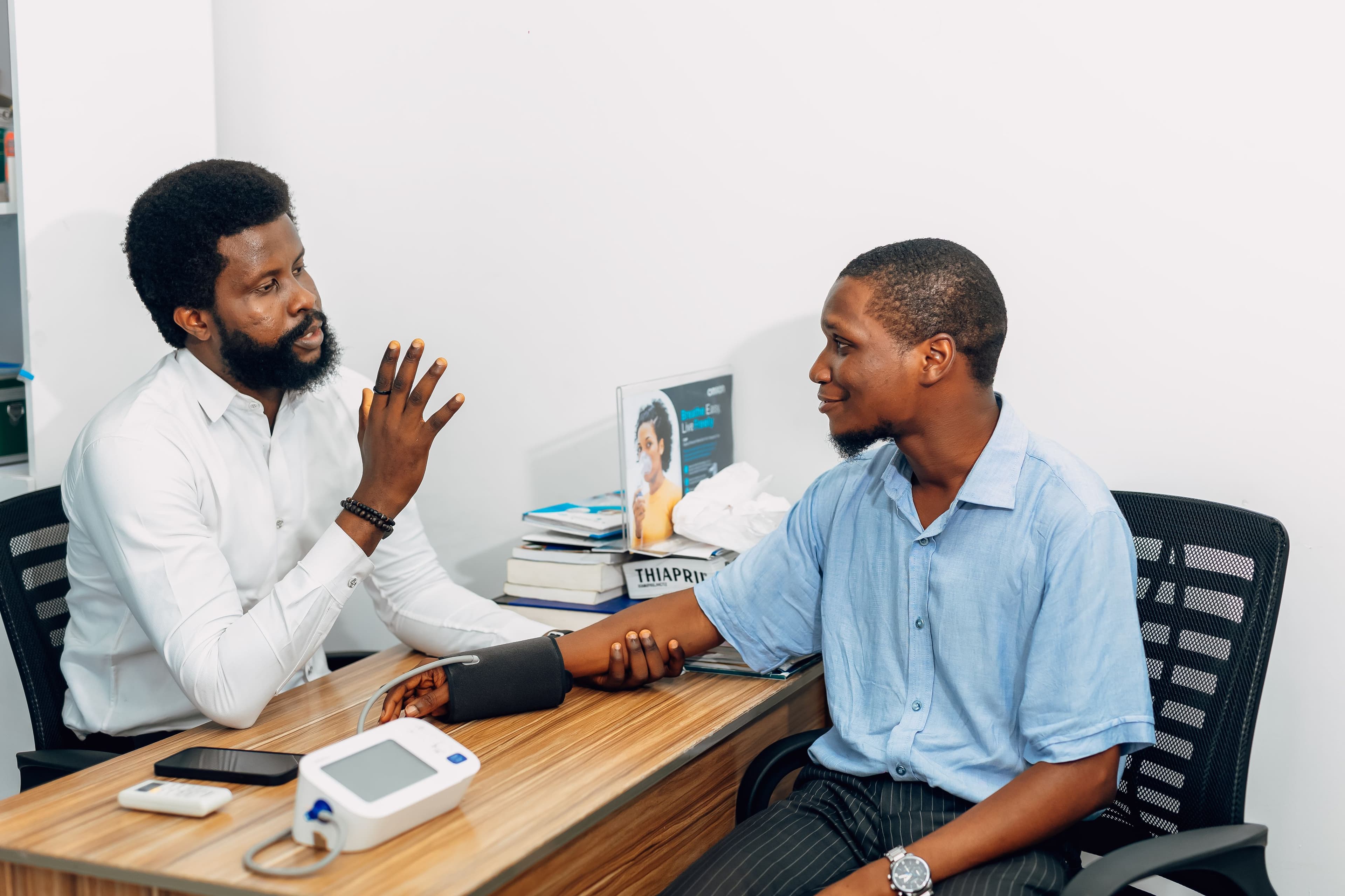 A healthcare professional in Lagos talks with a patient during a blood-pressure check. Demonstration photography, not a photograph of Beulah Group Hospital, its staff, or its facilities.
